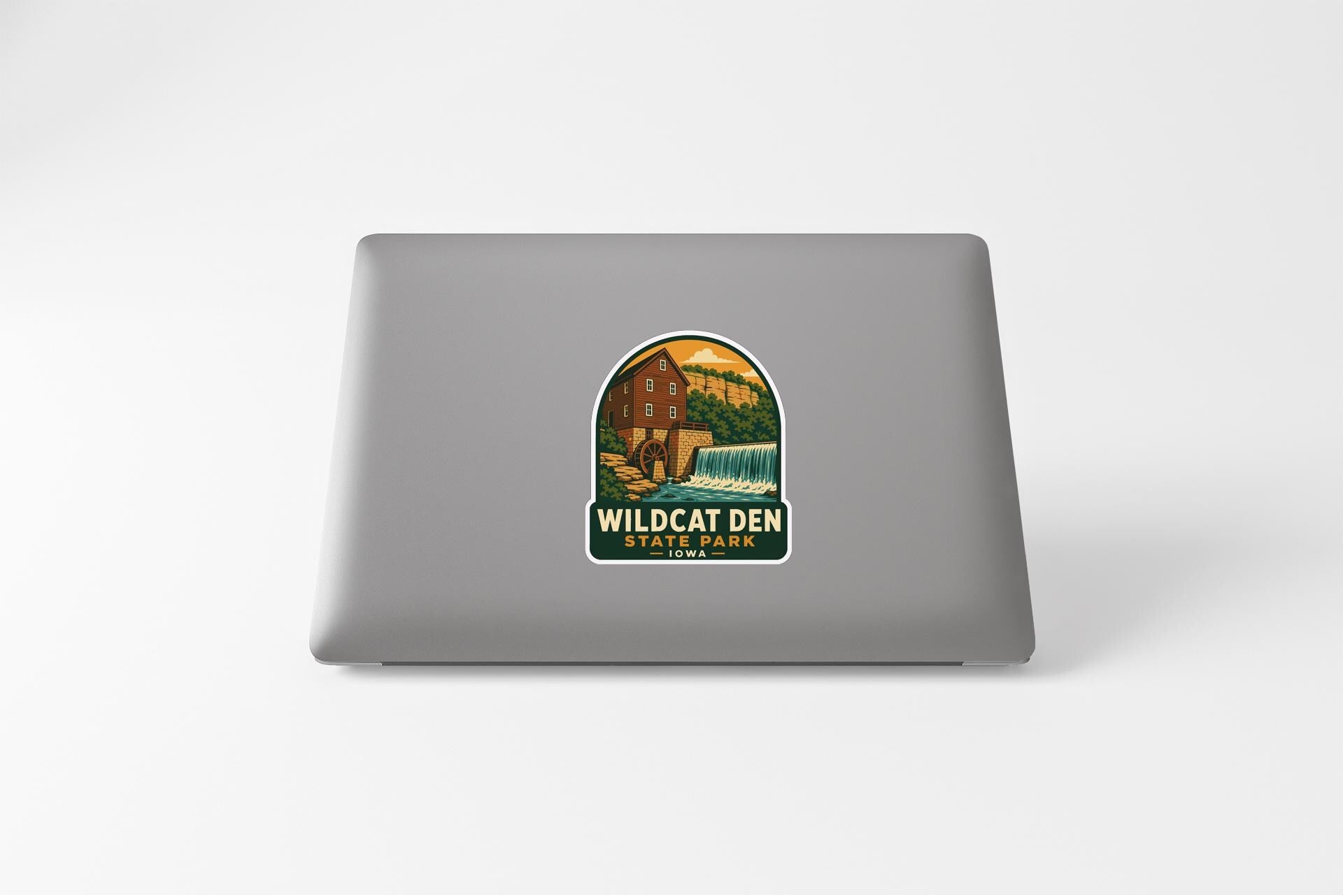 A sticker on the back of a laptop, depicting a scenic landscape with a building and a waterfall.