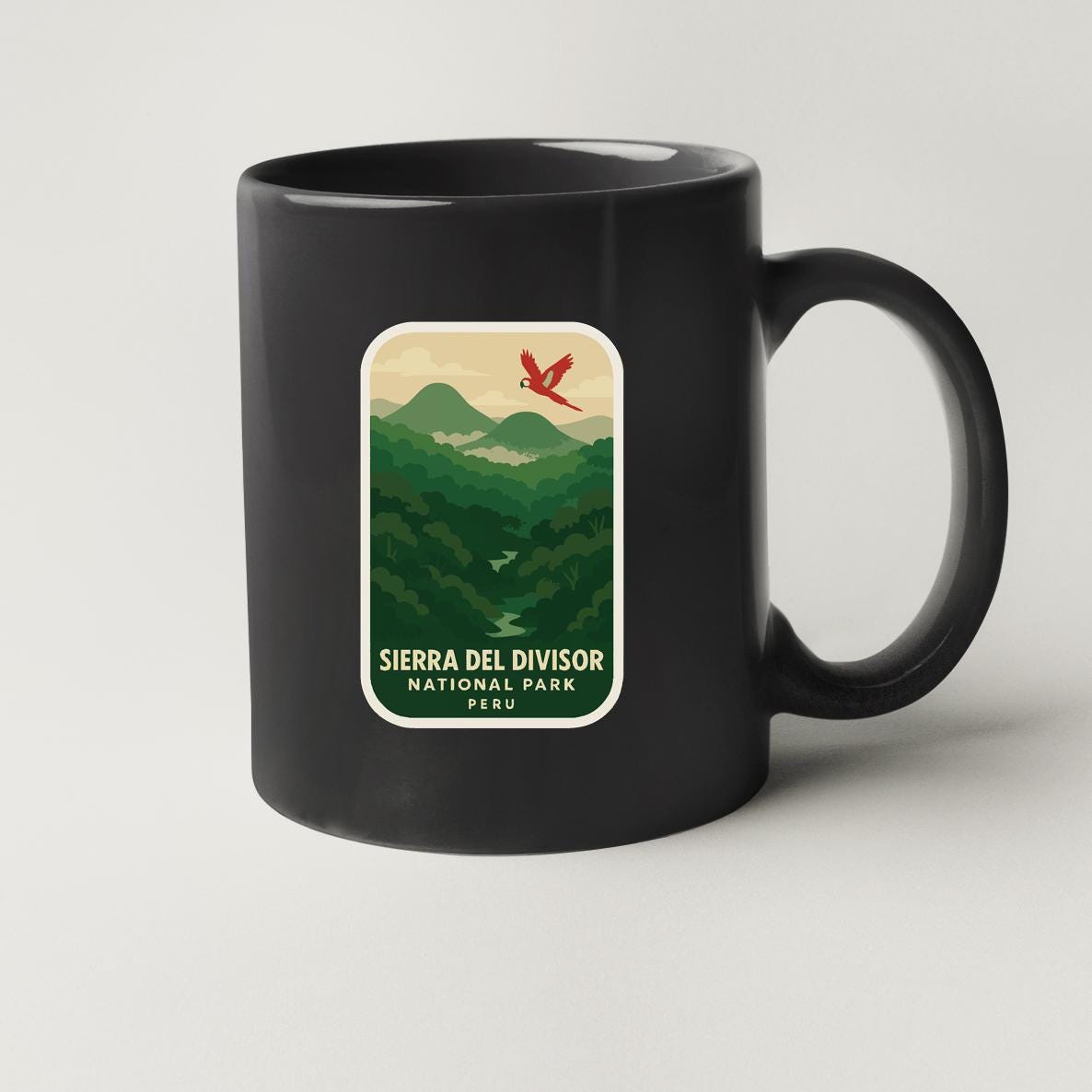 A black coffee mug with a graphic design depicting a mountain landscape and a red bird in flight.