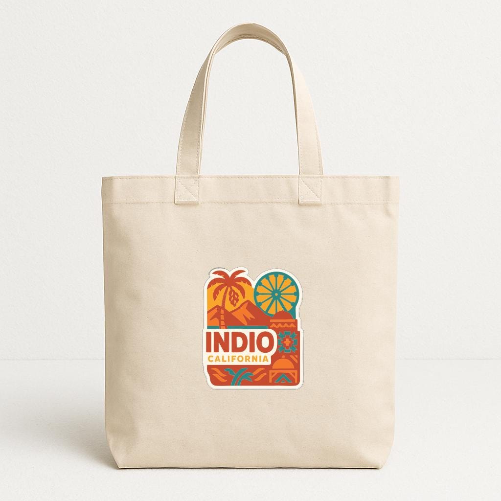 A beige tote bag with a colorful graphic design featuring palm trees, mountains, and the text "INDIO CALIFORNIA".