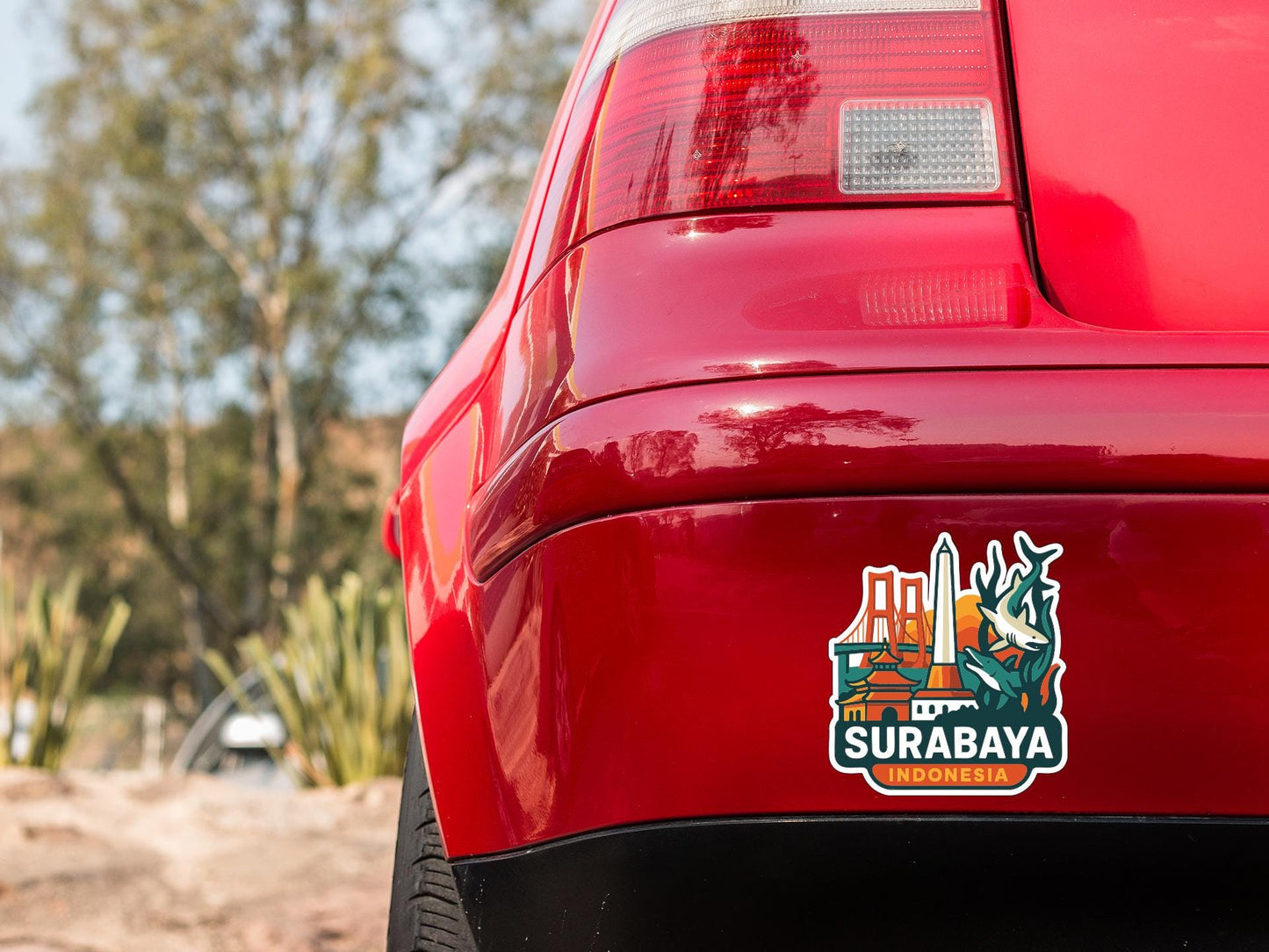 the rear end of a red car with a sticker on the trunk that says "SURABAYA" and "INDONESIA".