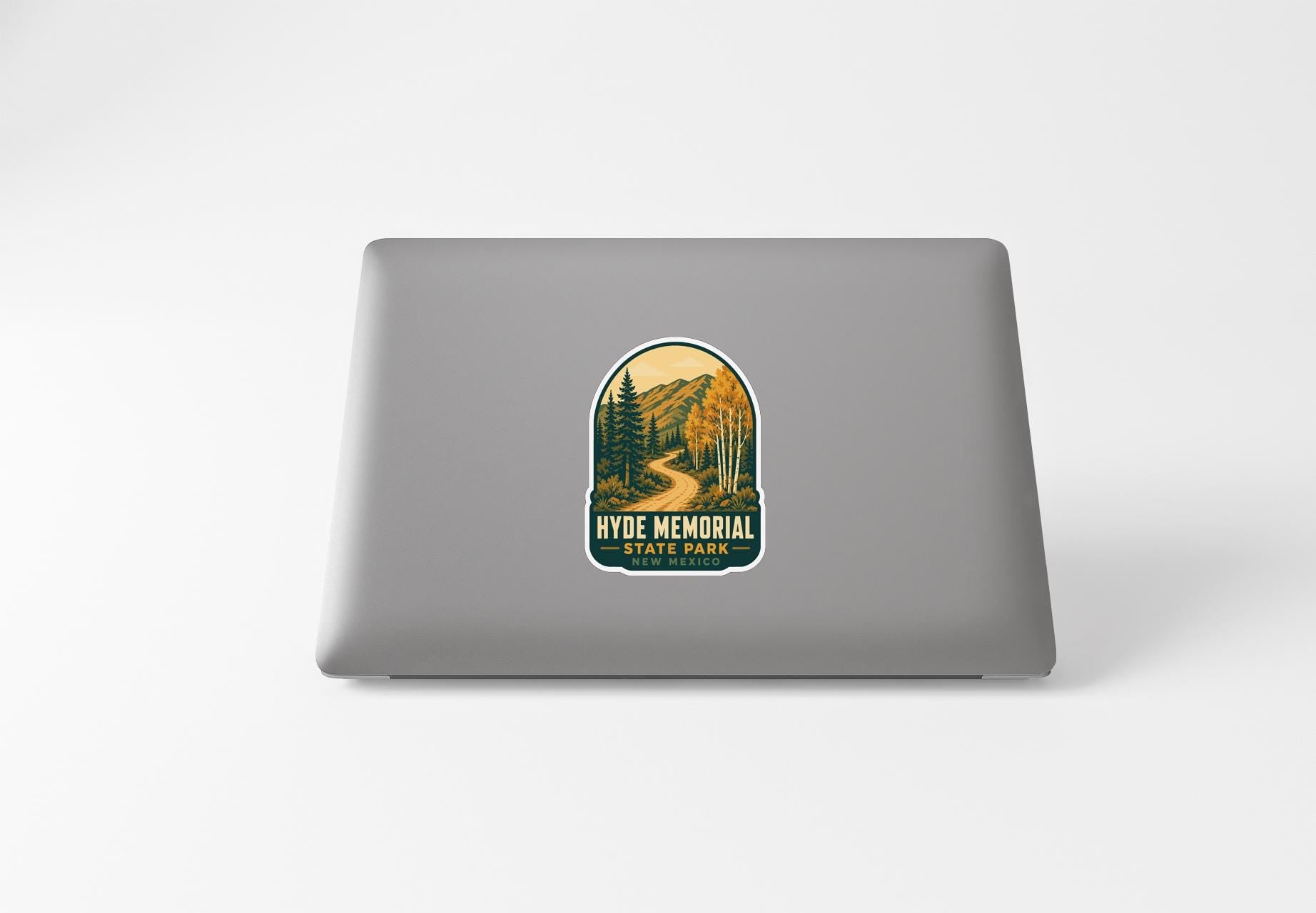 A sticker on the back of a laptop, depicting a scenic landscape with mountains, trees, and a winding road.