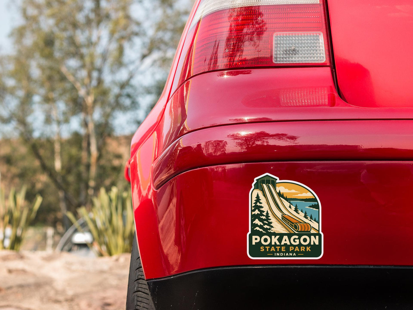 the rear end of a red car with a sticker on the back, featuring a scenic landscape with a mountain and a lake.