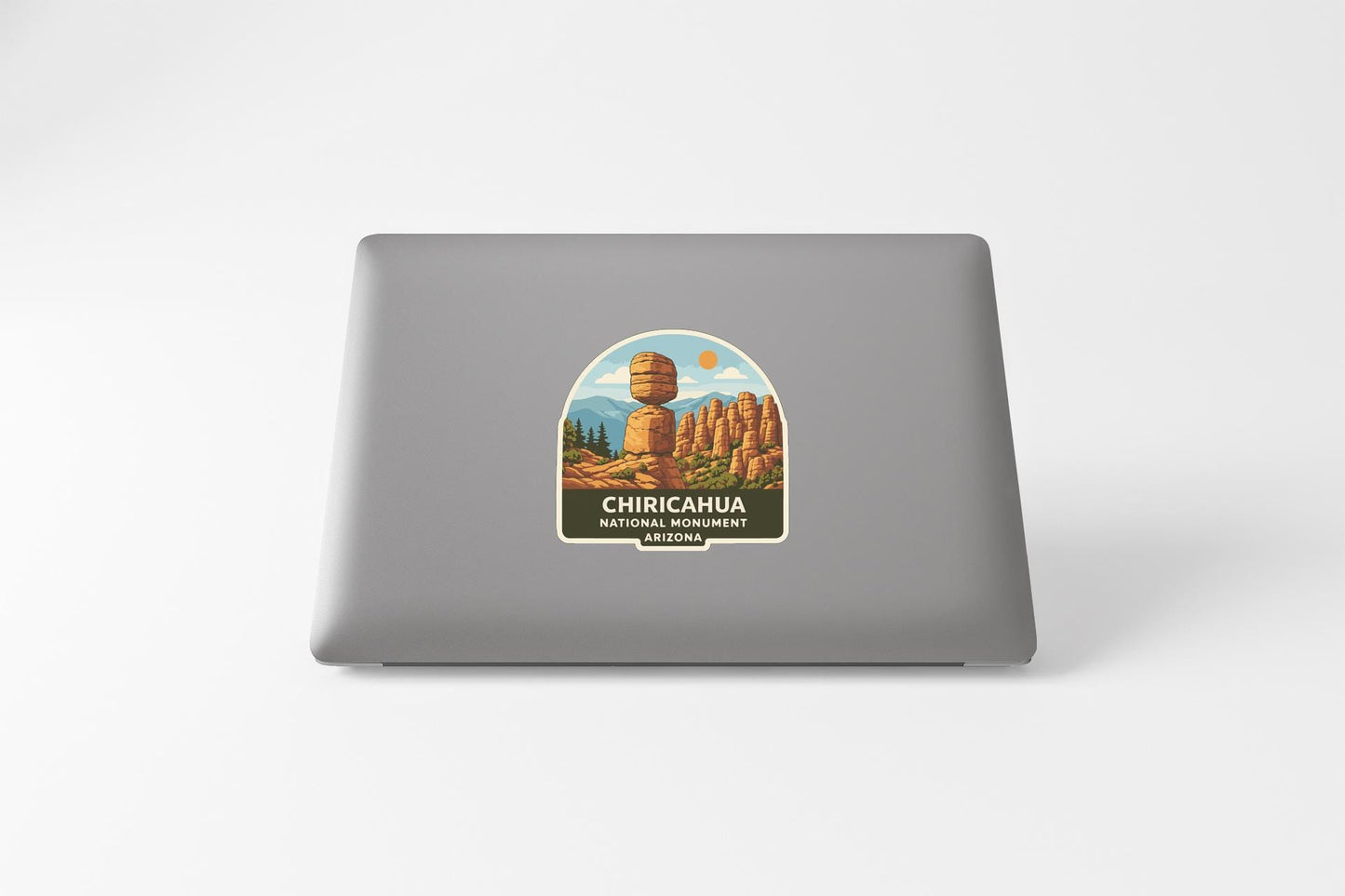 a sticker on the back of a laptop that displays a scenic landscape with mountains and a large rock formation.
