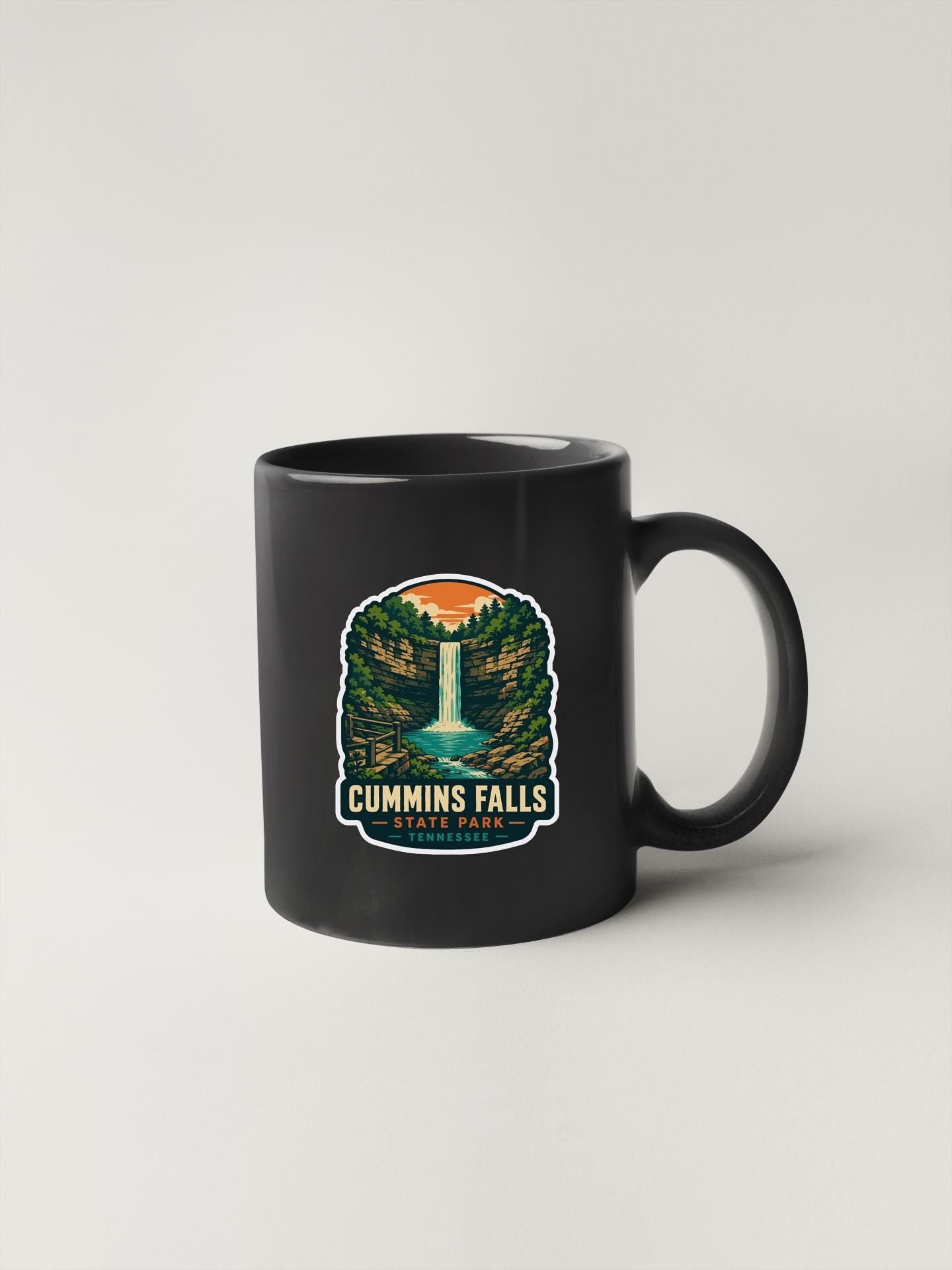 A black coffee mug with a graphic design depicting a waterfall and forest.
