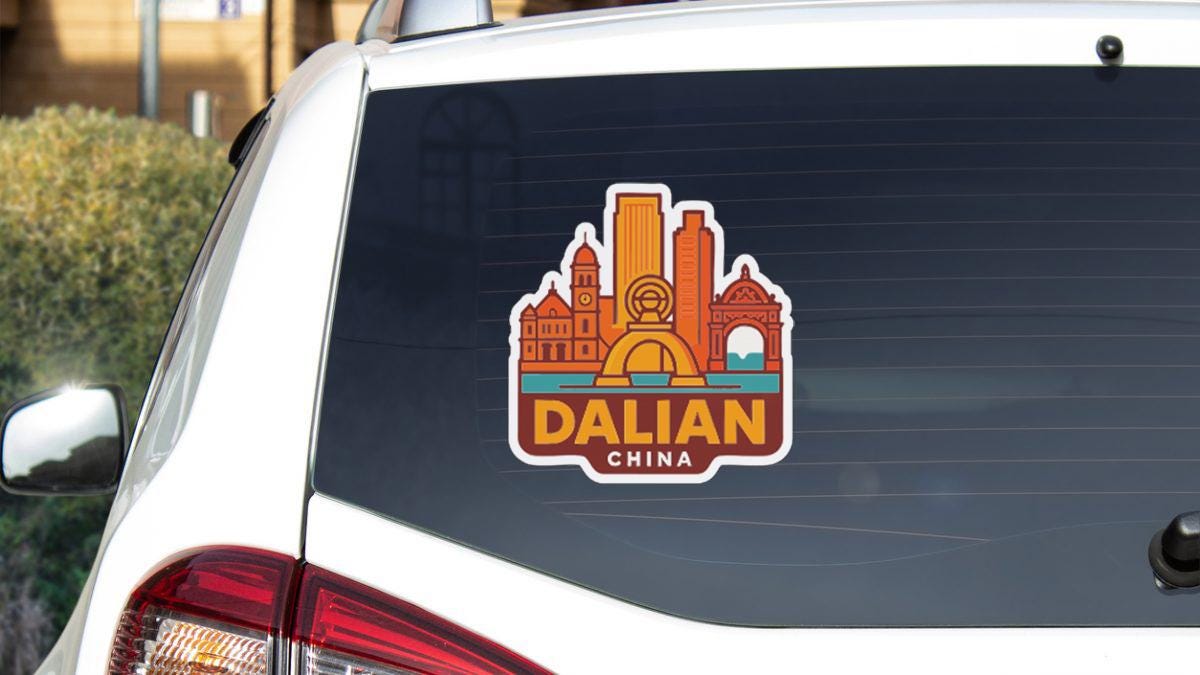 A sticker on the rear window of a white car, depicting a city skyline with the word "DALIAN" prominently displayed.
