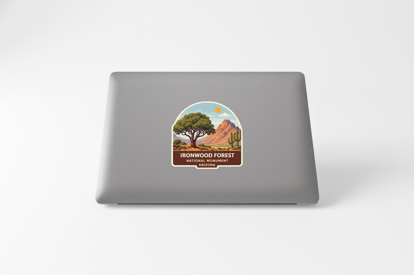a sticker on the back of a laptop that depicts a scenic landscape with a tree, mountains, and a clear sky.