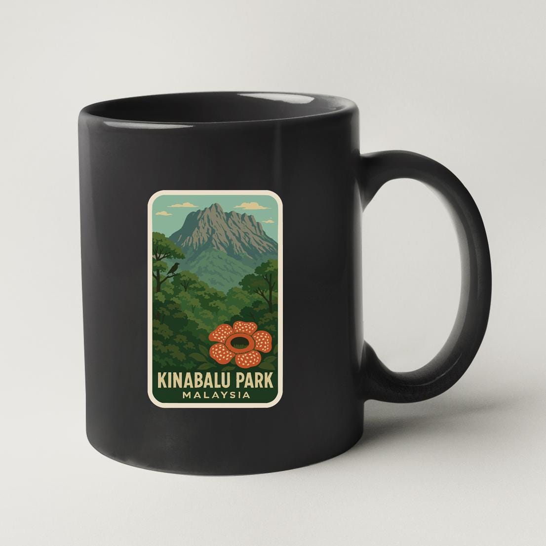 A black coffee mug with a sticker depicting a mountain landscape and a flower.