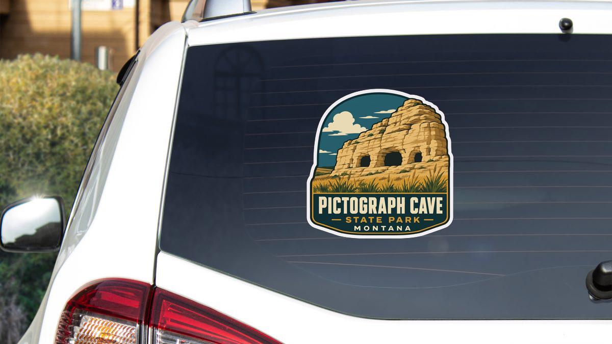 a sticker on the rear window of a white vehicle, depicting the Pictograph Cave State Park in Montana.