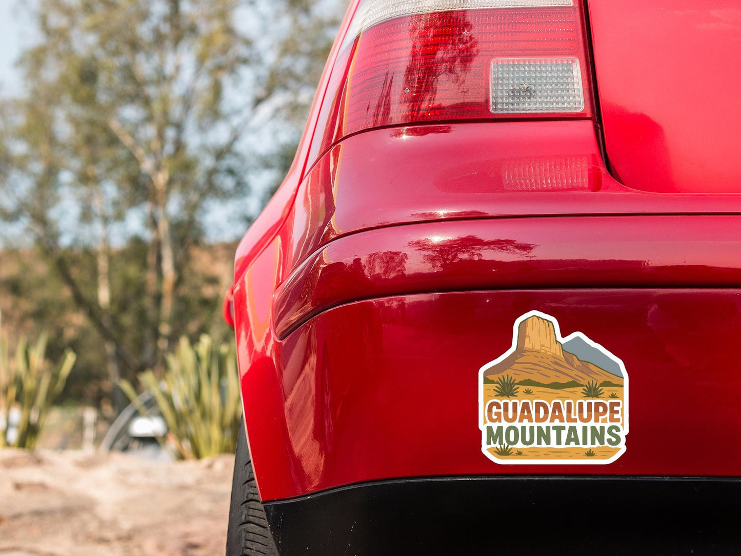 the rear end of a red car with a sticker on the trunk that says "GUADALUPE MOUNTAINS".