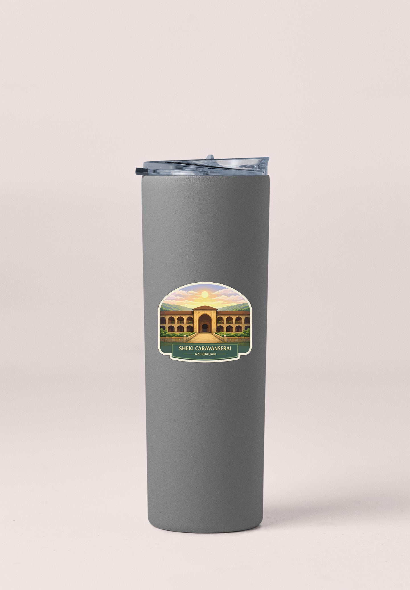A gray insulated tumbler with a lid and a sticker depicting a building with a sunset in the background.