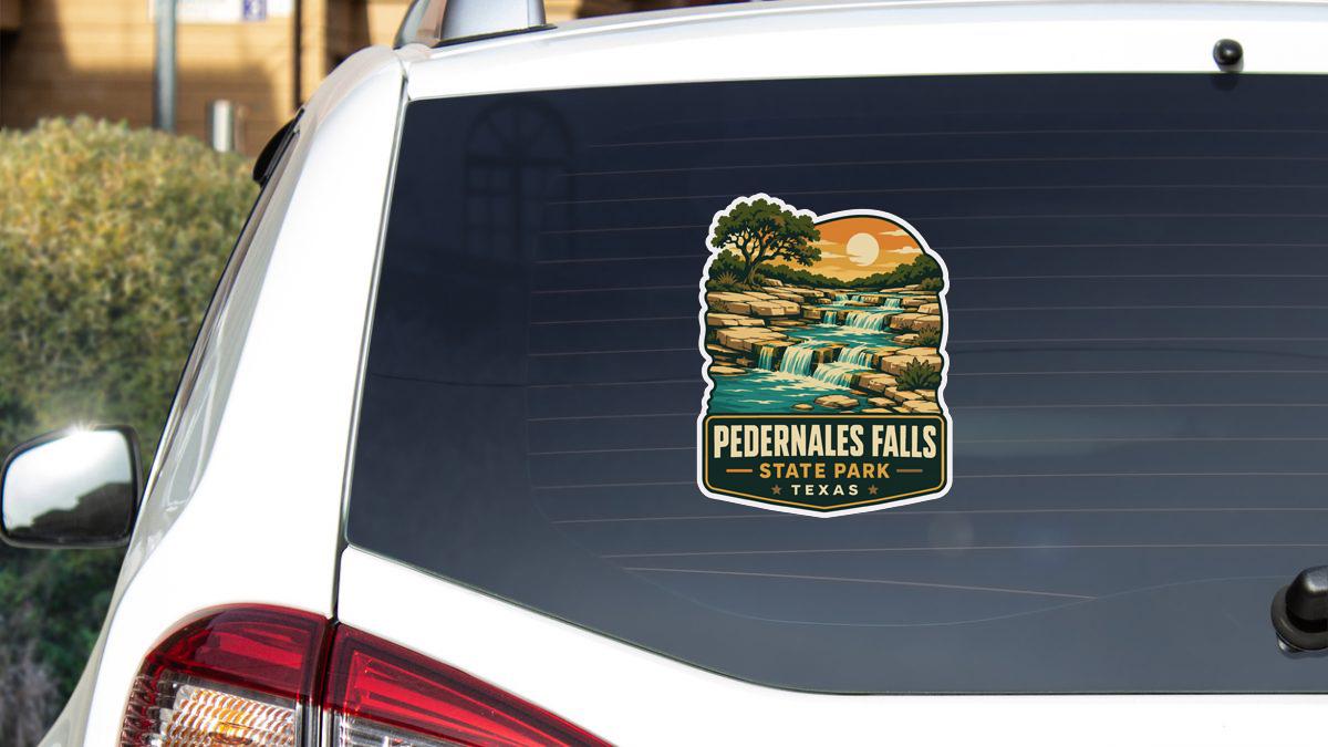 A sticker on the rear window of a white vehicle, depicting a scenic landscape with a waterfall and a sunset.