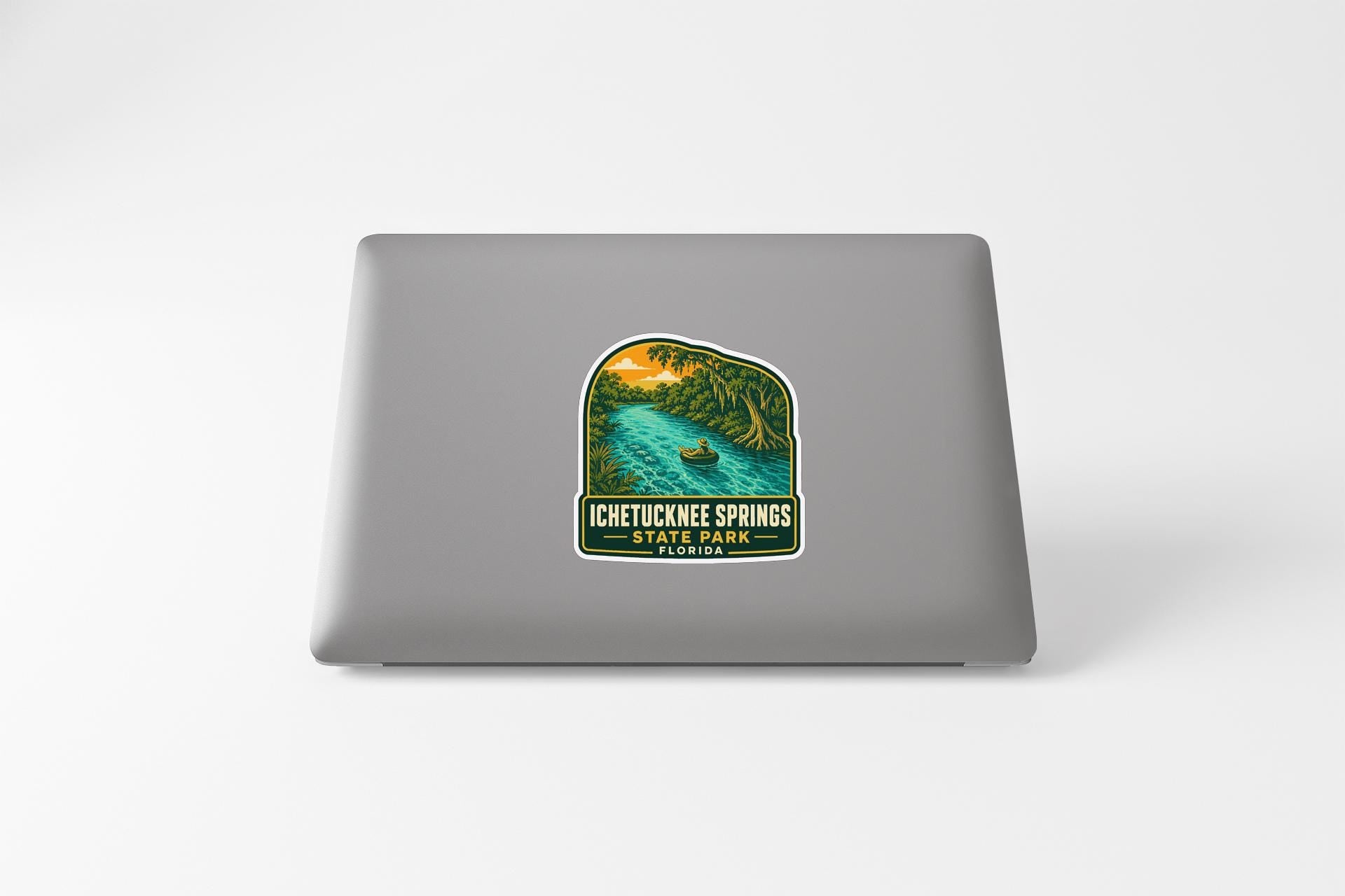 A sticker on the back of a laptop, depicting a scenic landscape with a river and a boat, along with the text "ICHETUCKEE SPRINGS STATE PARK".