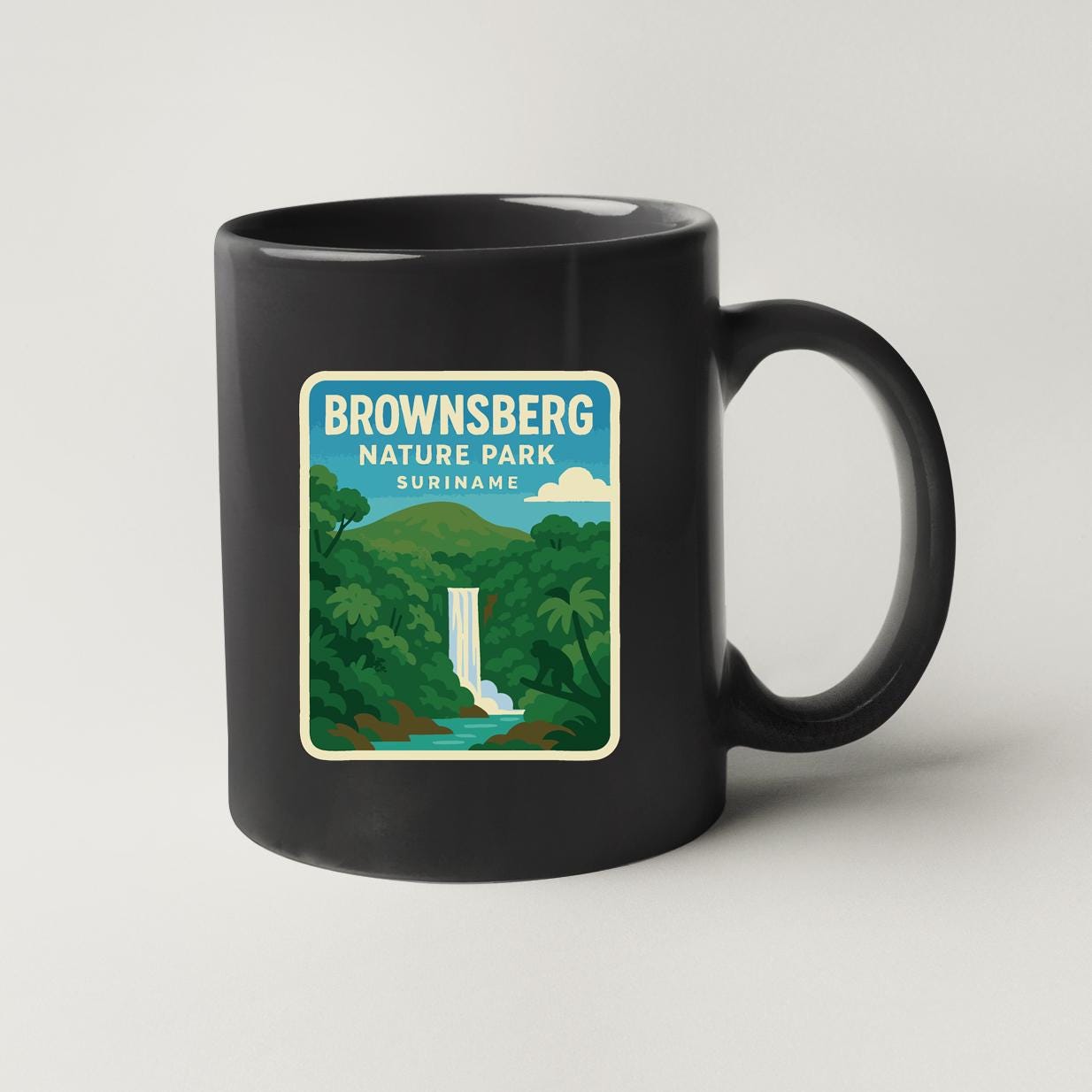 A black coffee mug with a sticker depicting a waterfall and lush greenery, representing the Brownsberg Nature Park in Suriname.
