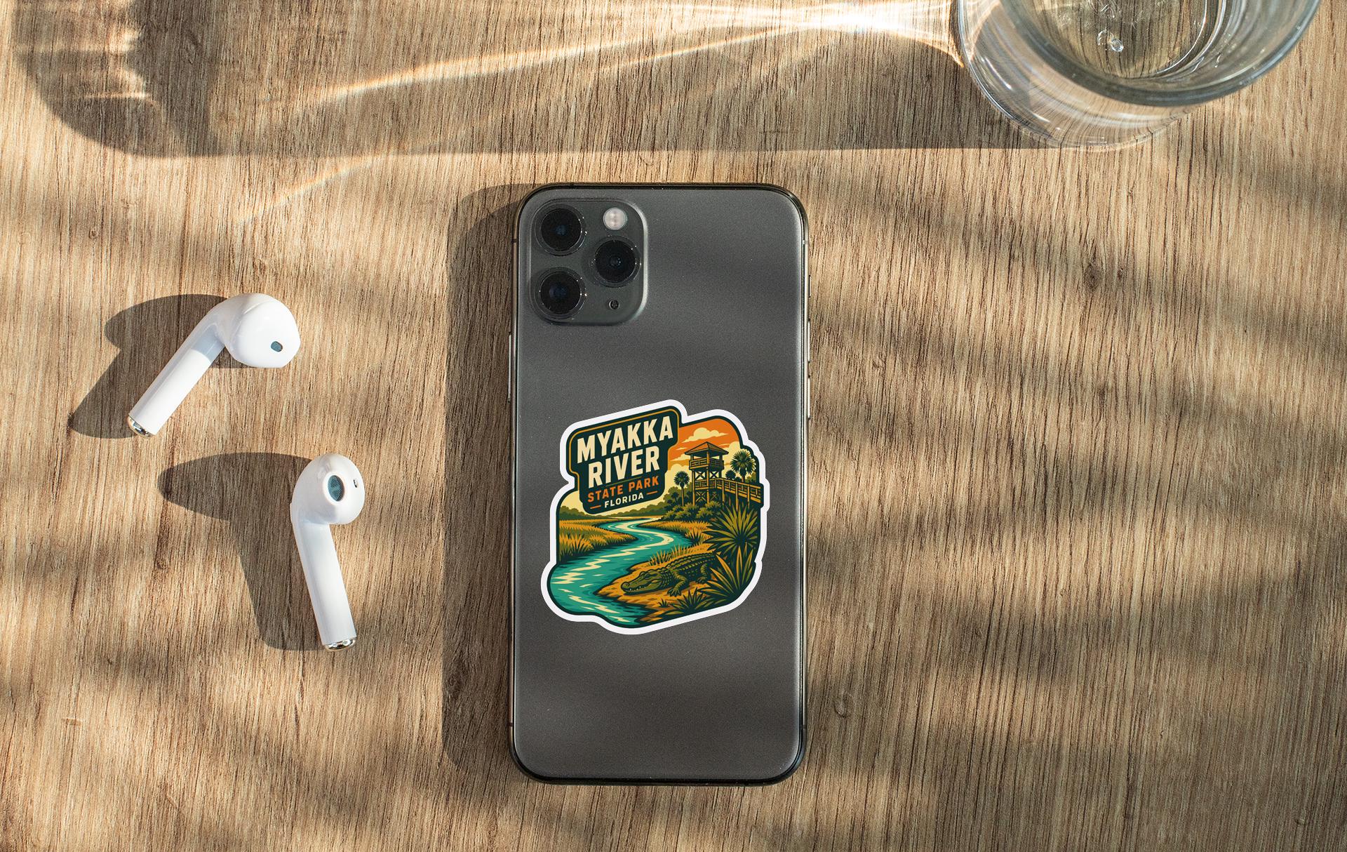 a smartphone with a sticker on the back, placed on a wooden surface alongside a pair of white earbuds and a glass of water.