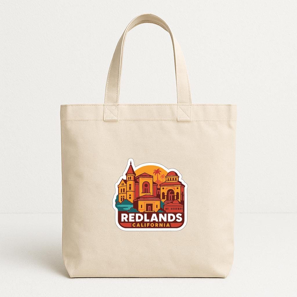 A beige tote bag with a colorful graphic of a cityscape and the text "REDLANDS, CALIFORNIA" printed on it.