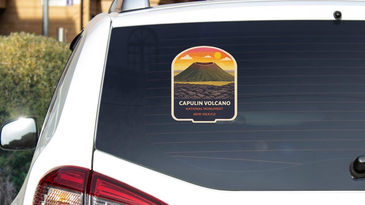 A sticker on the rear window of a white car that says "Capulin Volcano National Monument NEW MEXICO".