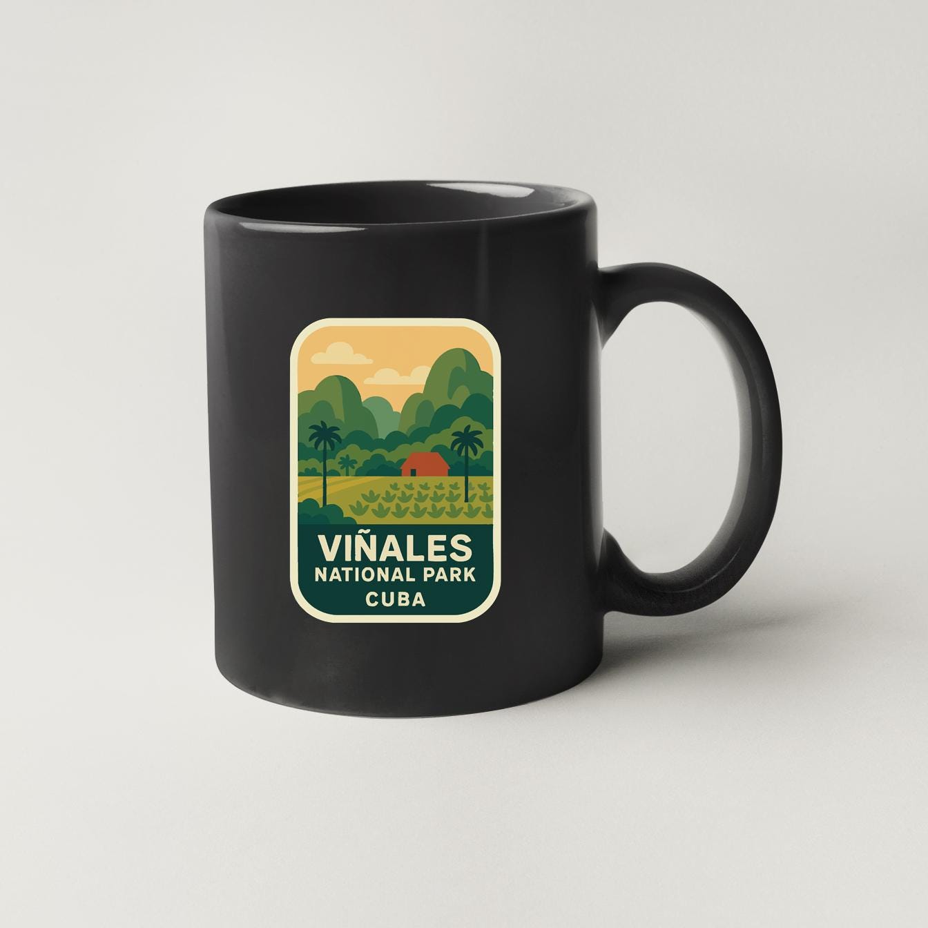A black coffee mug with a graphic design depicting a tropical landscape, including palm trees, mountains, and a small red building.