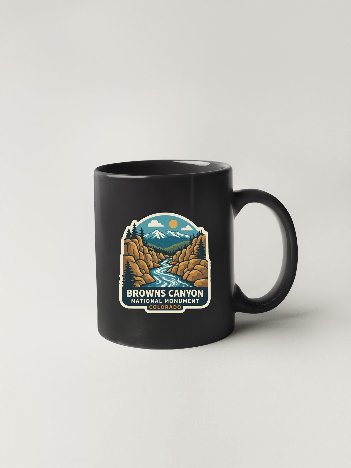 A black coffee mug with a label that says "Browns Canyon National Monument, Colorado" and features an illustration of a mountain landscape.
