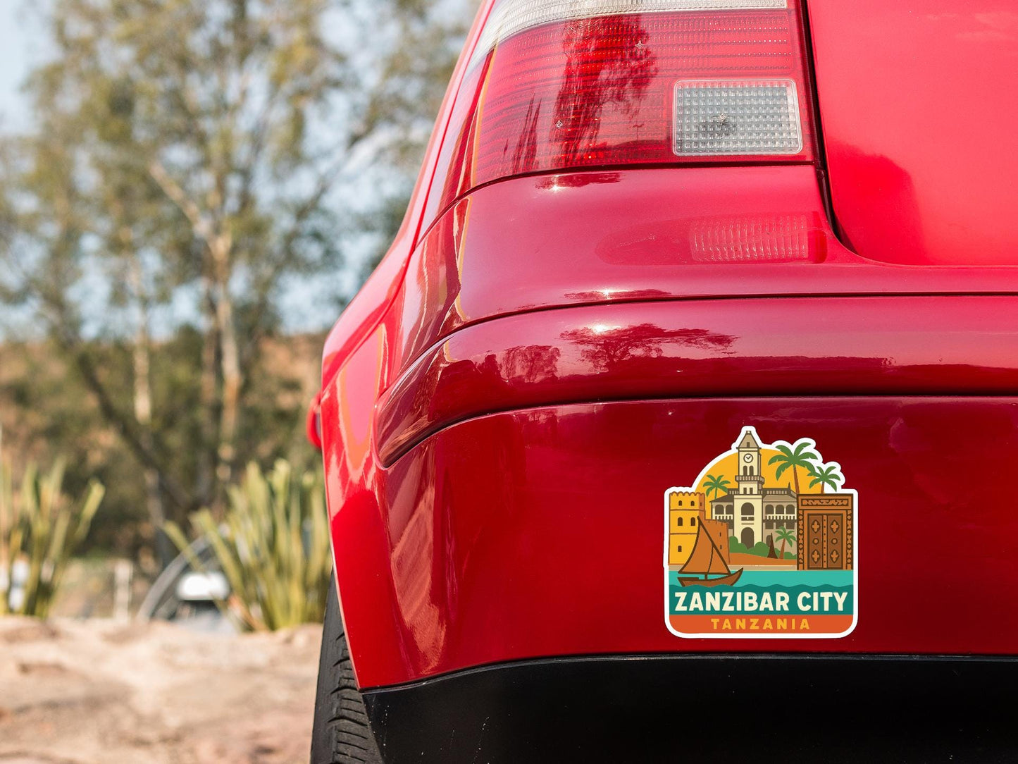 the rear end of a red car with a sticker on the trunk that features a cityscape and text.