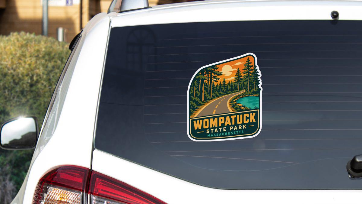 A sticker on the rear window of a white car, depicting a scenic road leading to Wompatuck State Park in Massachusetts.