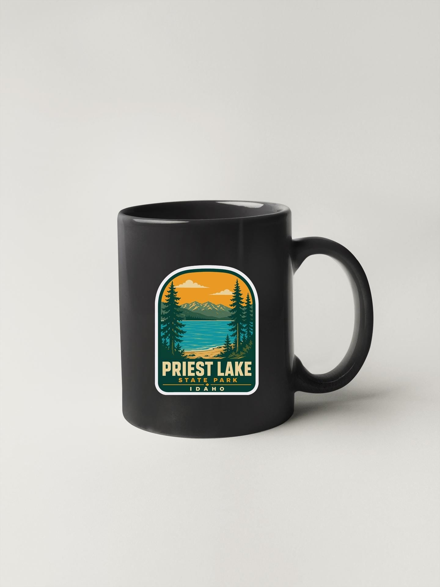 A black coffee mug with a graphic design depicting a scenic landscape featuring a lake, mountains, and pine trees.