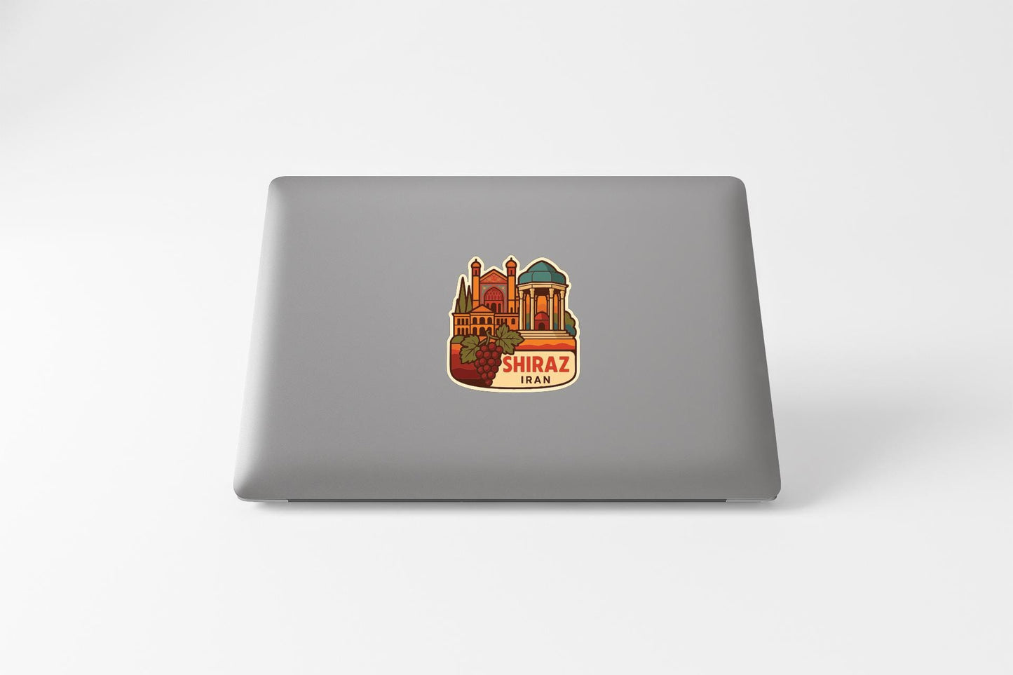 A sticker depicting a building with a dome and the text "SHIRAZ IRAN" on it, placed on the back of a laptop.