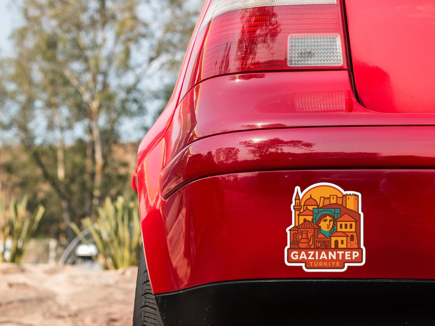 the rear end of a red car with a sticker on the trunk that features a cartoon-style illustration of a person and buildings.
