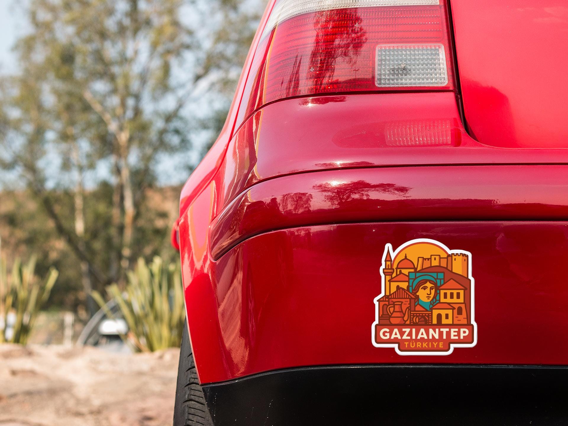 the rear end of a red car with a sticker on the trunk that features a cartoon-style illustration of a person and buildings.