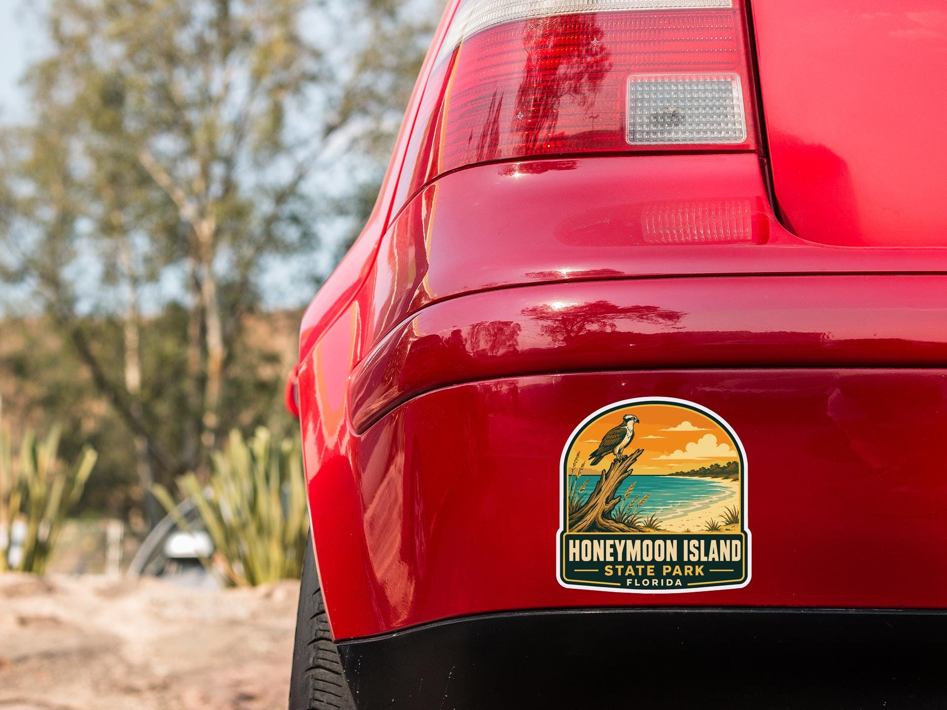 the rear end of a red car with a sticker on the back window that says "Honeymoon Island State Park, Florida".
