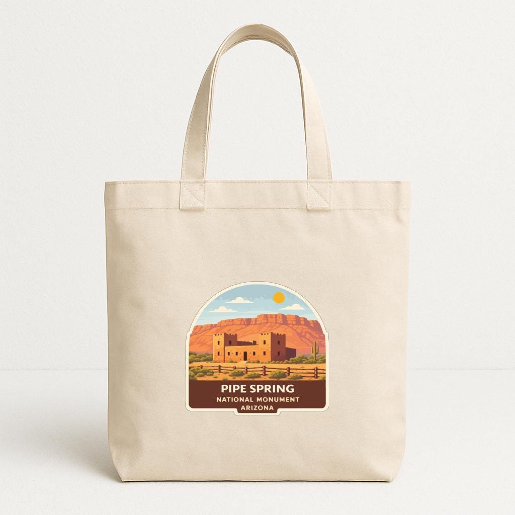 A beige tote bag with a label that features an illustration of the iconic landmark, Pipe Spring National Monument in Arizona.