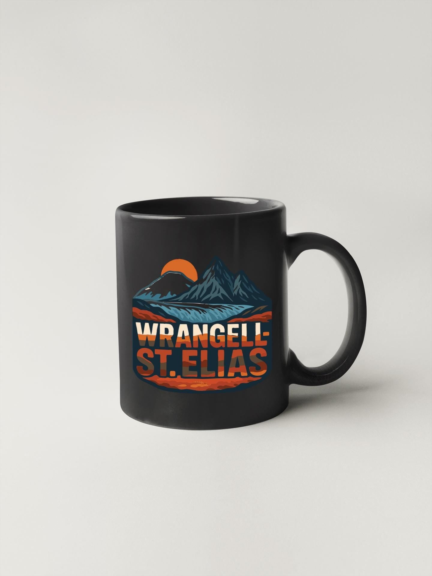 A black coffee mug with a graphic design featuring mountains, a sunset, and the text "WRANGELI ST. ELIAS".