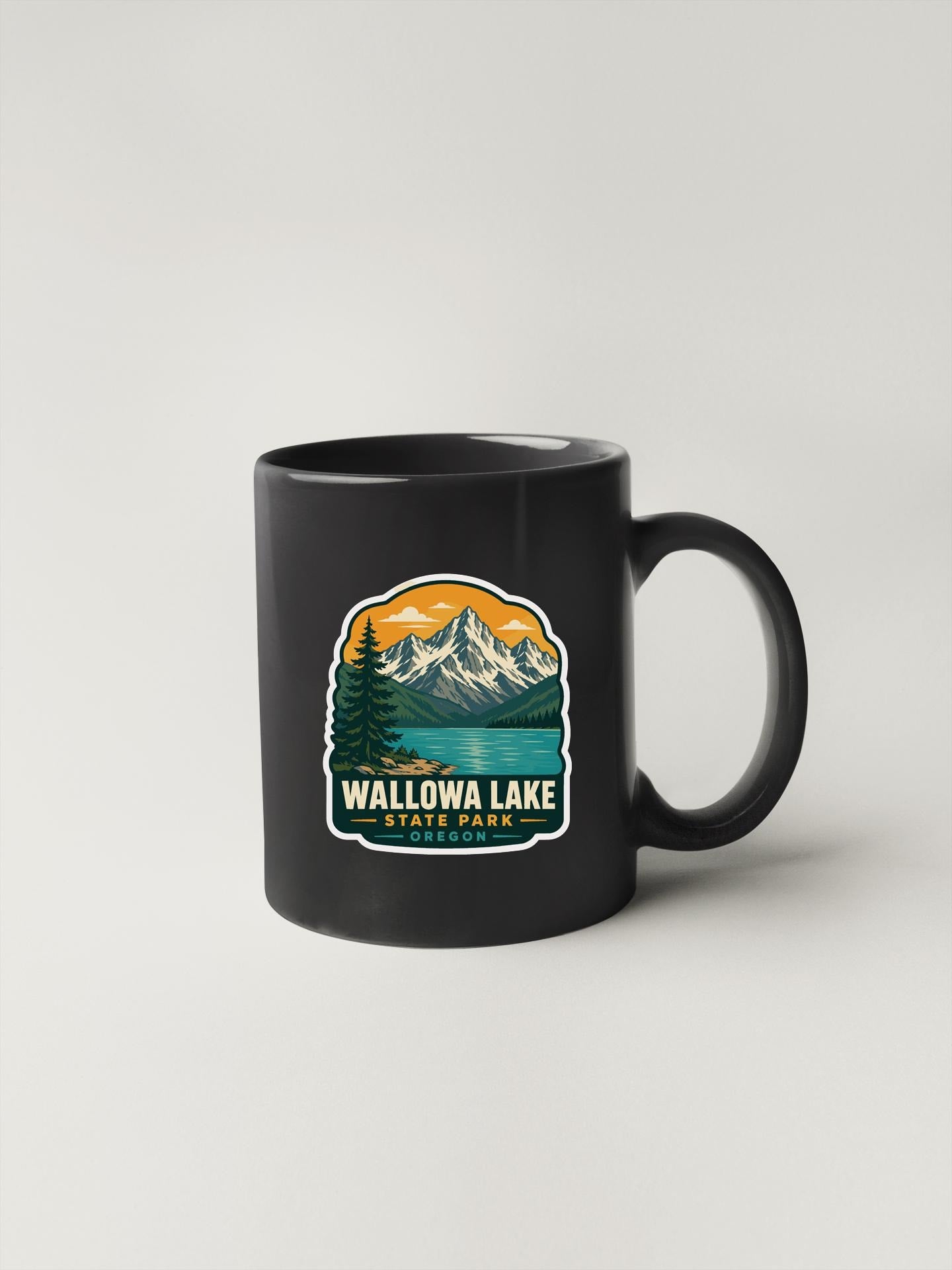 A black coffee mug with a graphic design depicting a mountain landscape and a lake, along with the text "Wallowa Lake State Park".