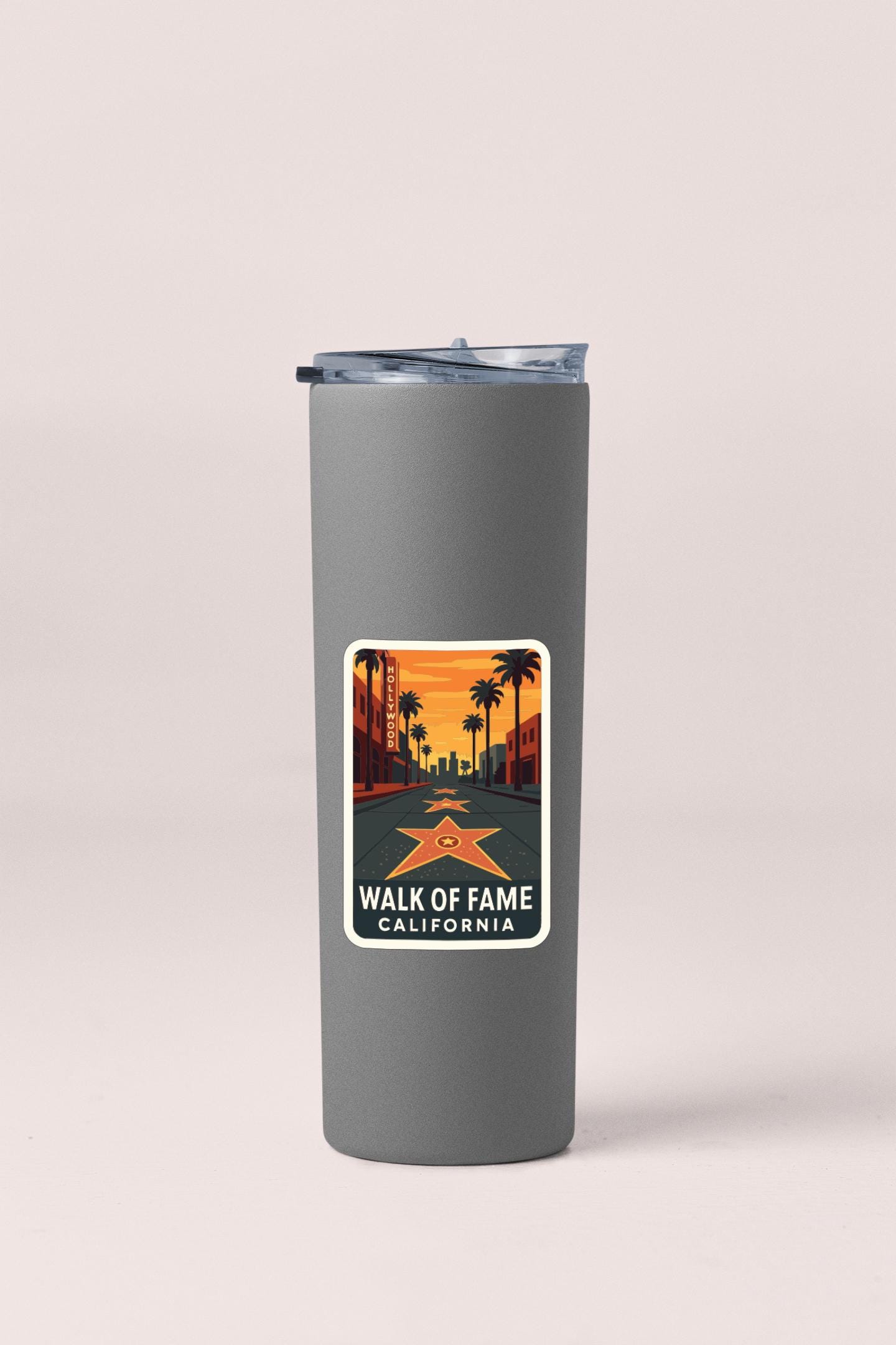 A gray insulated tumbler with a sticker on it depicting a sunset over a city street with palm trees.