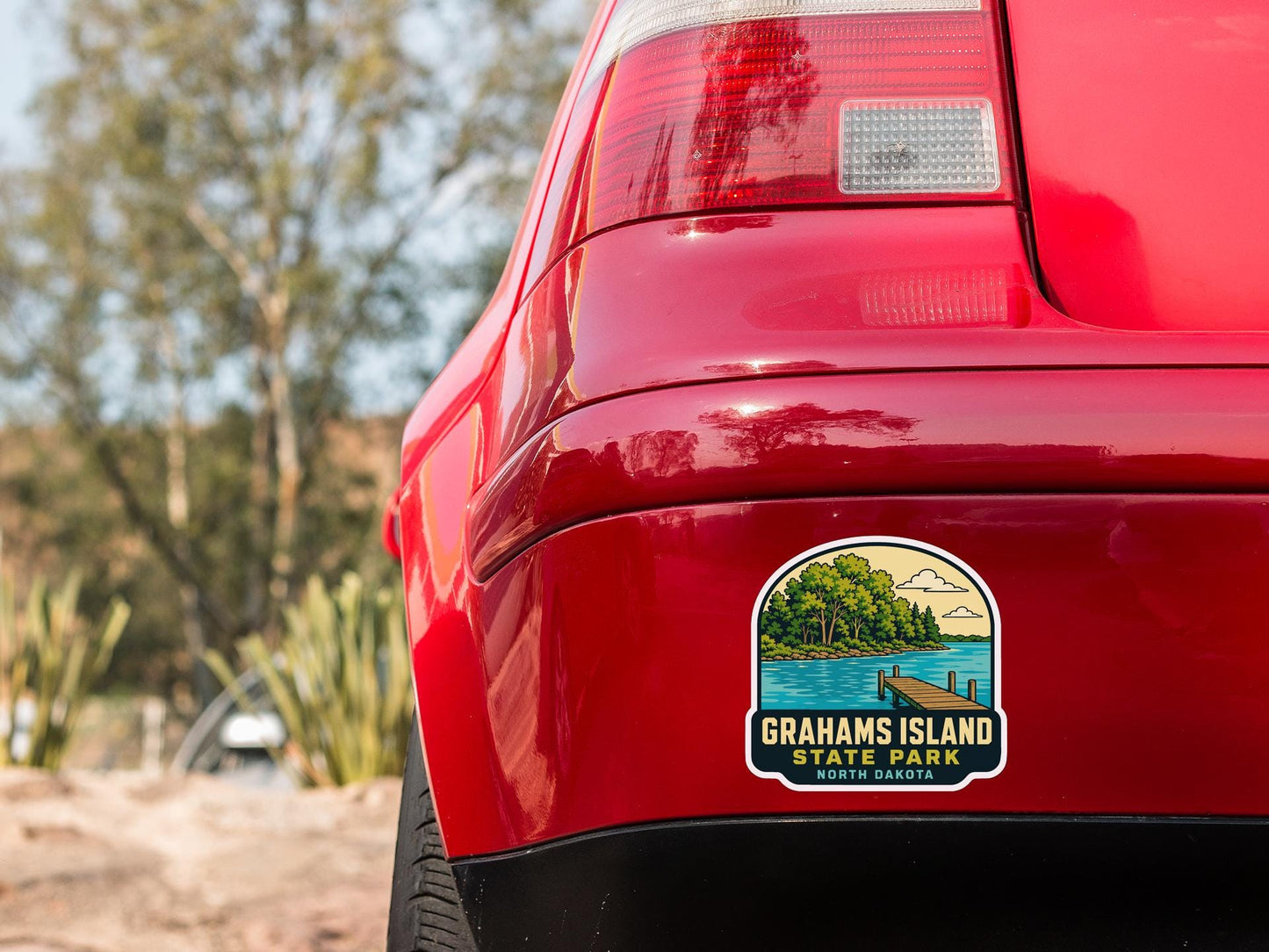 the rear end of a red car with a sticker on the back window that says "Grahms Island State Park North Dakota".