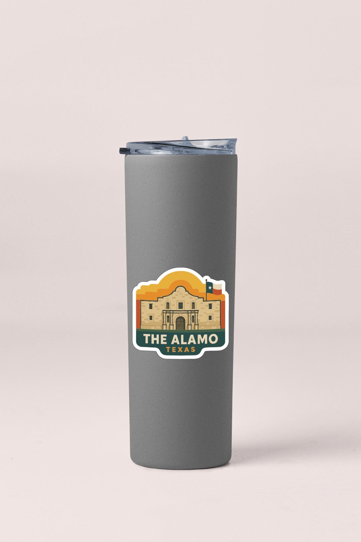 A gray insulated tumbler with a sticker depicting the Alamo, a historic landmark in Texas.