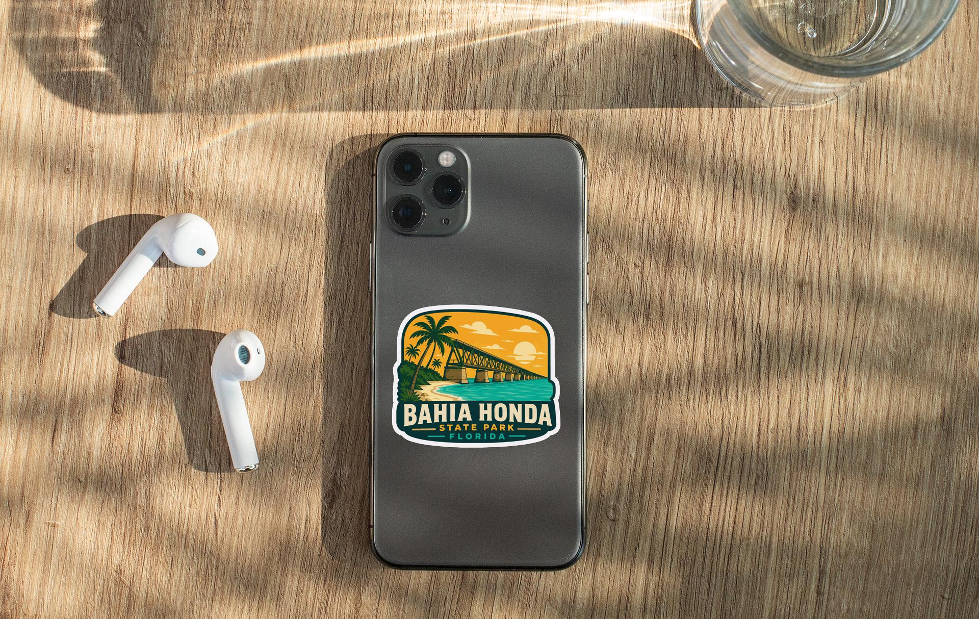 a smartphone with a sticker on it, along with a pair of white earbuds and a glass of water on a wooden surface.