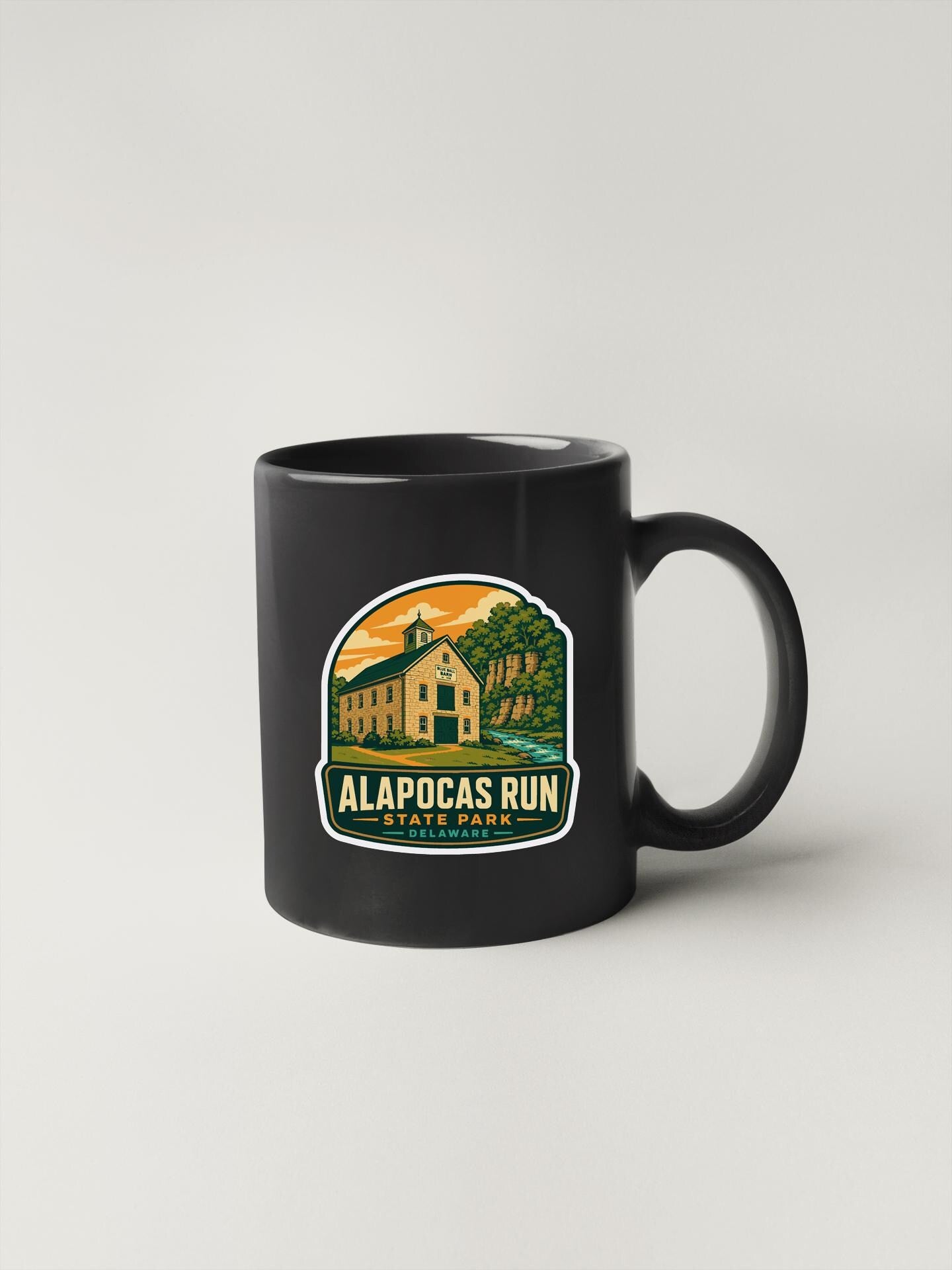 A black coffee mug with a graphic design depicting a house and trees, along with the text "ALAPOCAS RUN STATE PARK DELAWARE" printed on it.