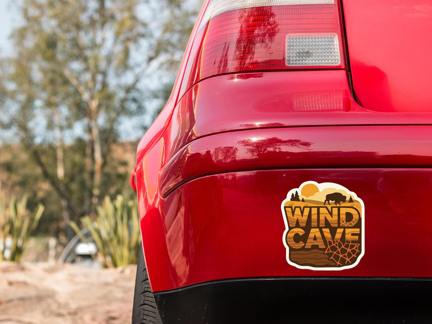 the rear end of a red car with a sticker on the trunk that says "WIND CAVE".