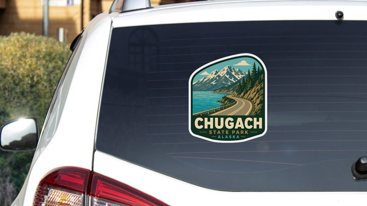 A sticker on the rear window of a white car, depicting a scenic mountain landscape with a winding road and a body of water.