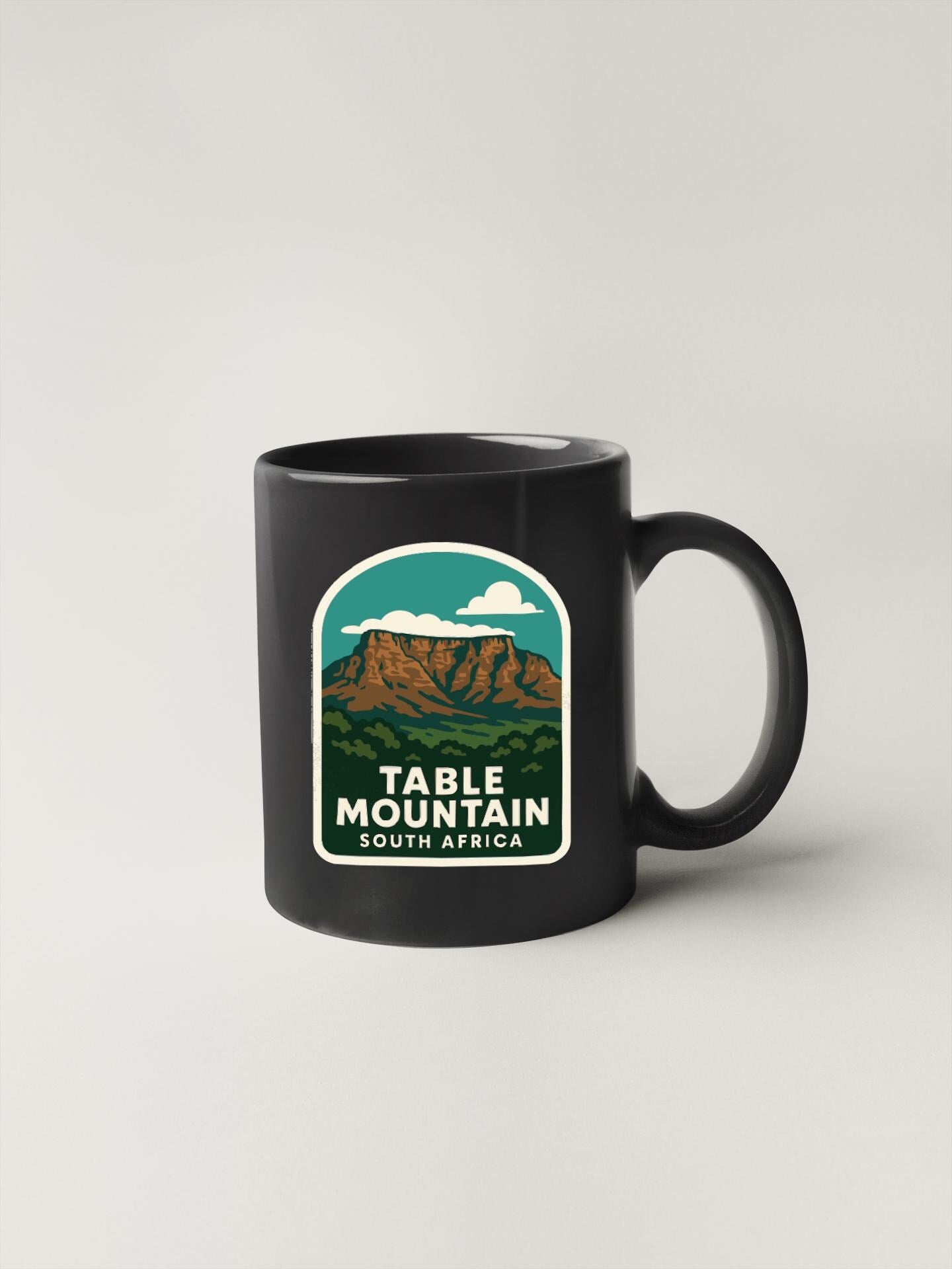 A black coffee mug with a graphic design depicting Table Mountain in South Africa.