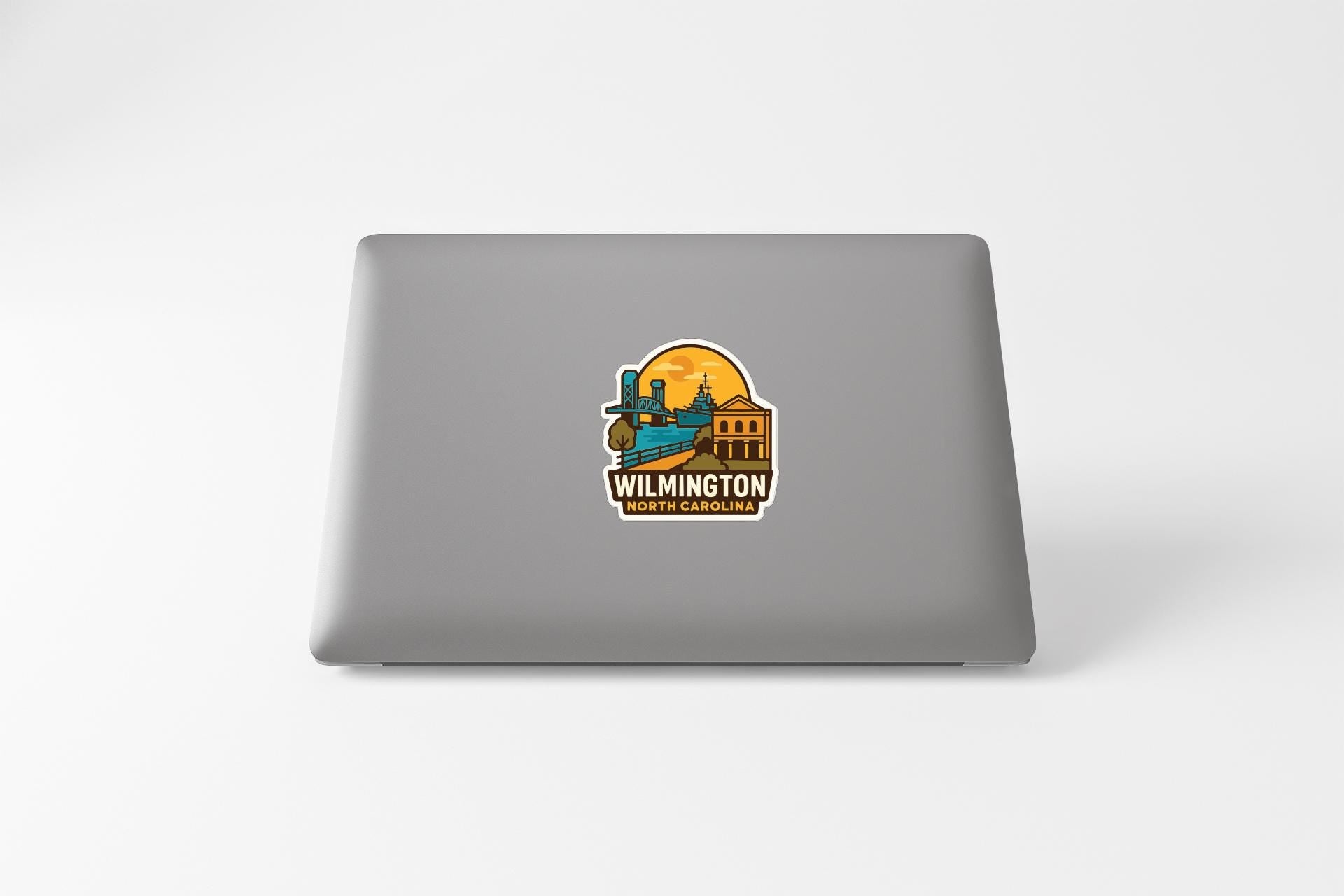 A sticker on the back of a laptop displaying the text "WILMINGTON NORTH CAROLINA" along with an illustration of a building and a boat.