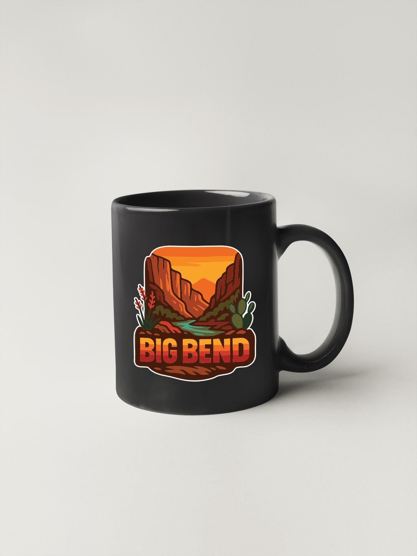 A black coffee mug with a graphic design depicting a desert landscape with mountains, cacti, and a river. The text "BIG BEND" is displayed prominently on the mug.