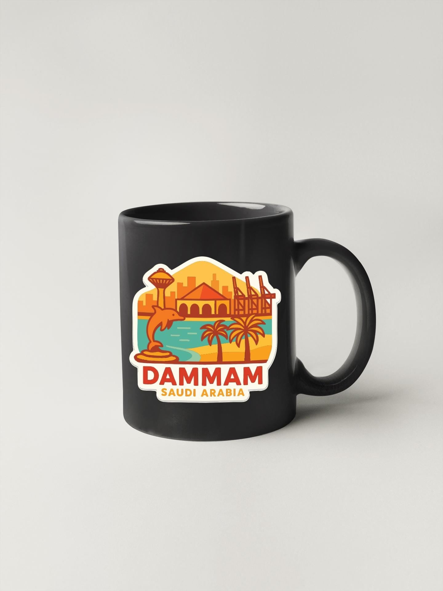 A black coffee mug with a colorful sticker depicting a cityscape and palm trees, along with the text "DAMMAM SAUDI ARABIA".
