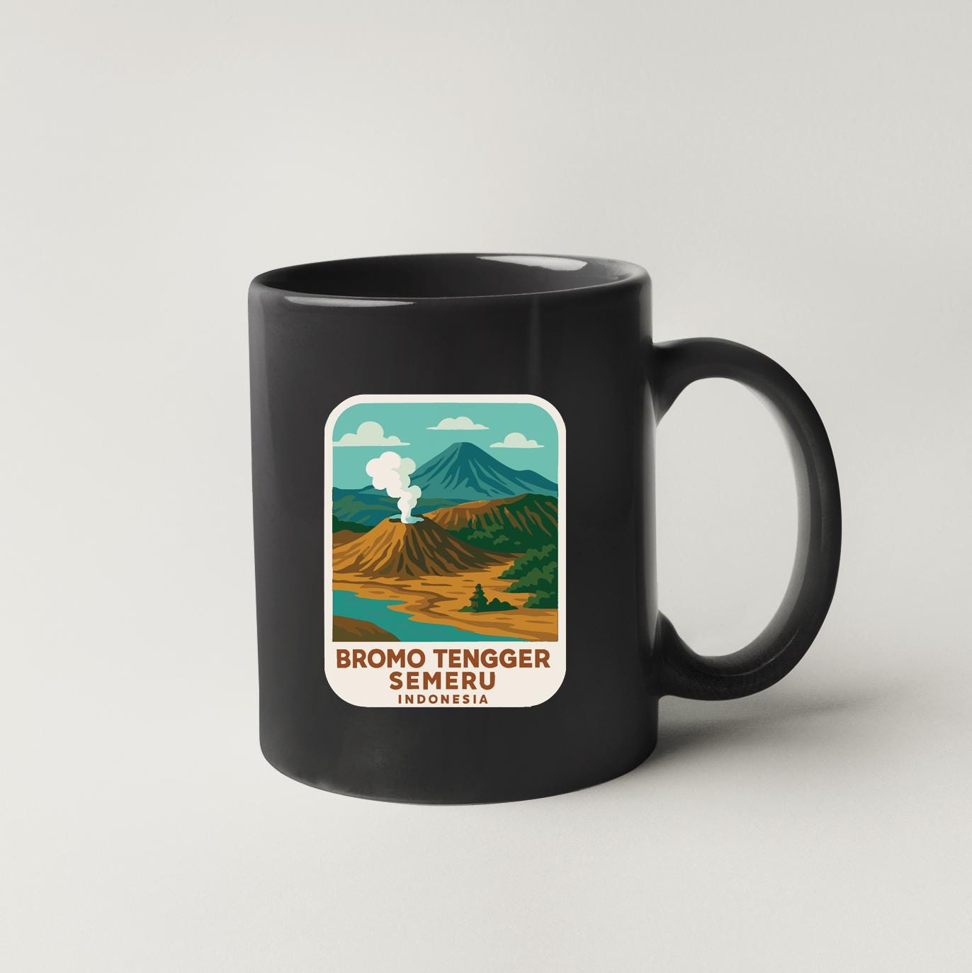 A black coffee mug with a sticker depicting a scenic landscape with mountains, a volcano, and a body of water.