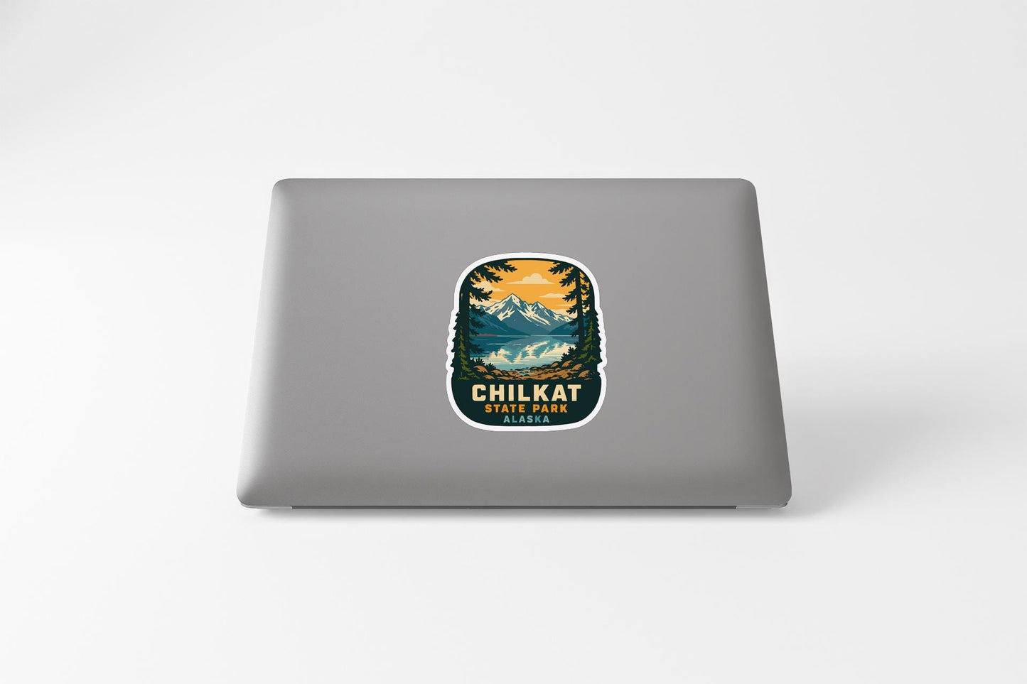 A sticker on the back of a laptop, depicting a scenic mountain landscape with a lake and trees.