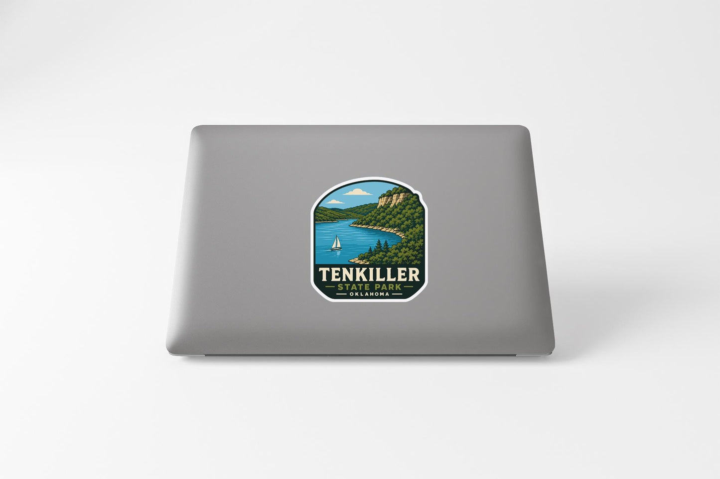 A sticker on the back of a laptop, depicting a scenic landscape with a lake, mountains, and a sailboat.
