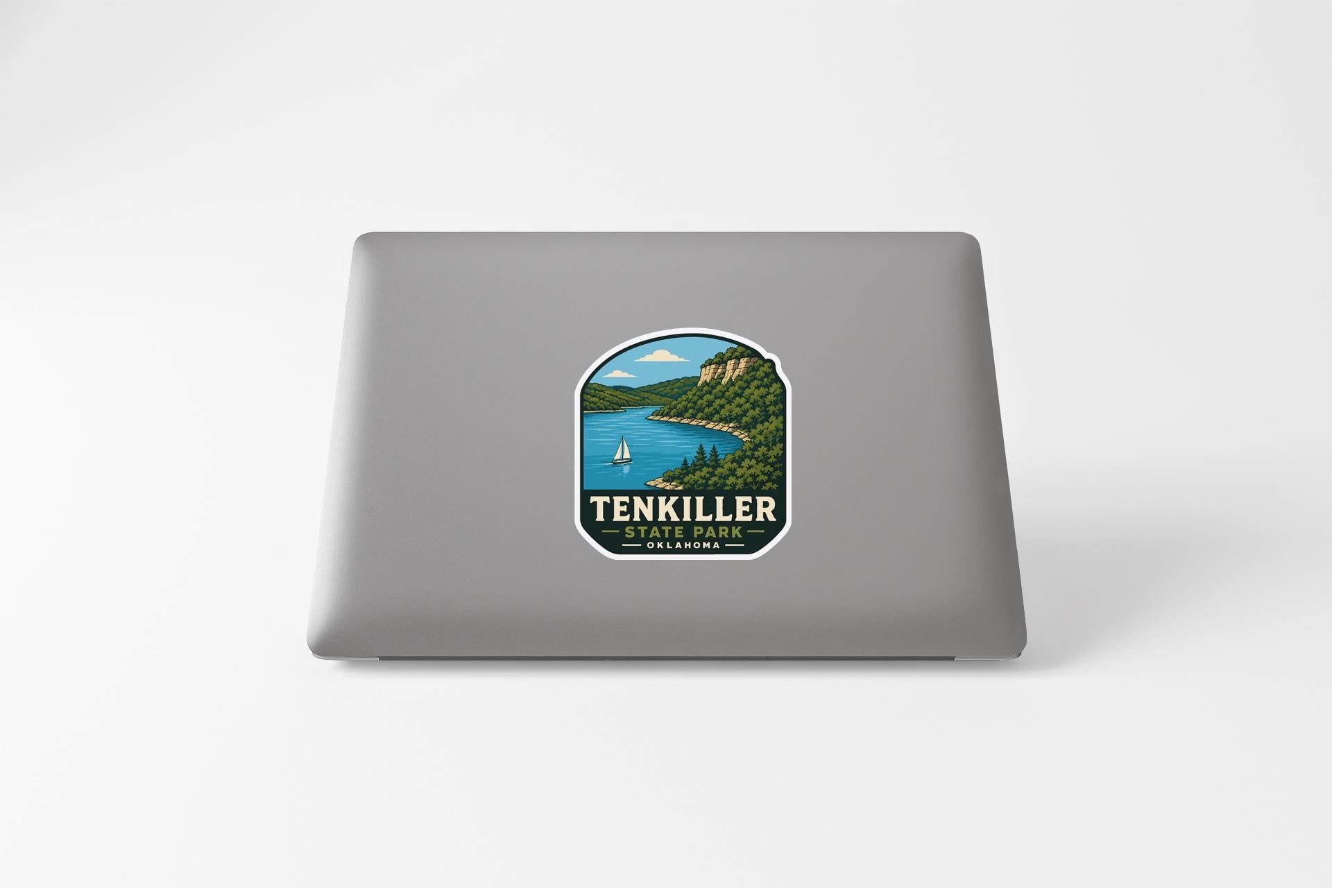A sticker on the back of a laptop, depicting a scenic landscape with a lake, mountains, and a sailboat.