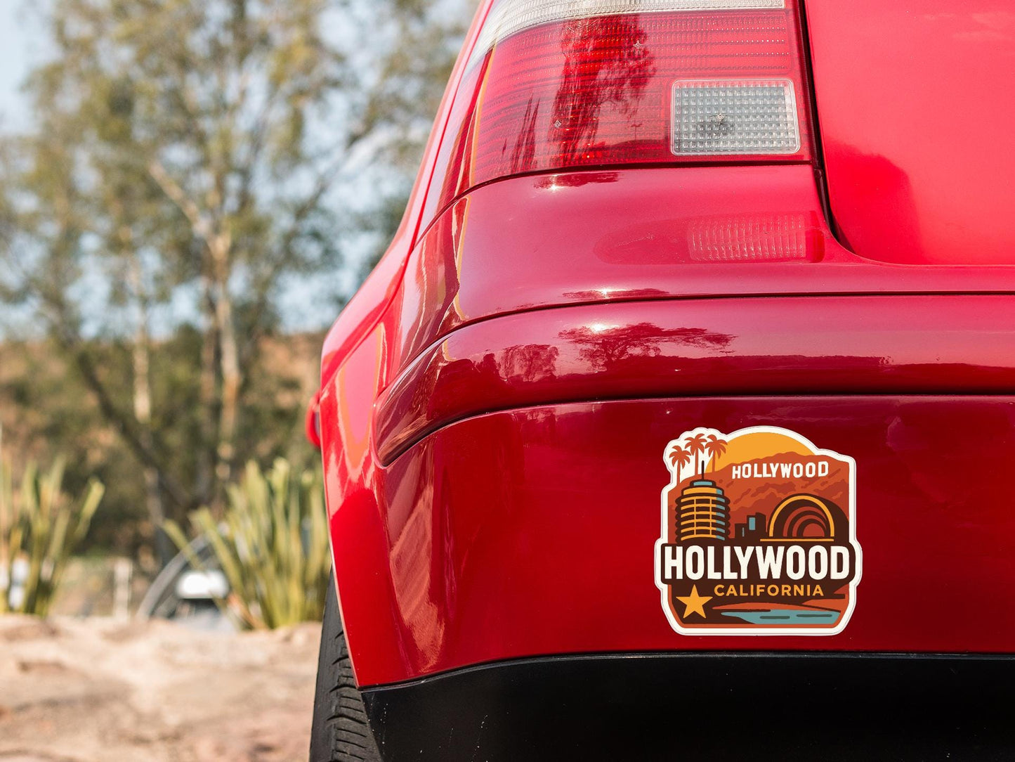 the rear end of a red car with a sticker on the trunk that says "Hollywood California".
