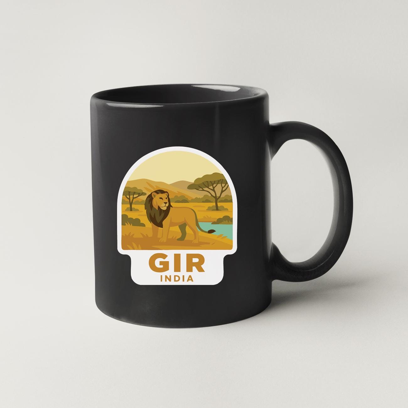 A black coffee mug with a sticker depicting a lion in a savanna landscape and the text "GIR INDIA" below it.