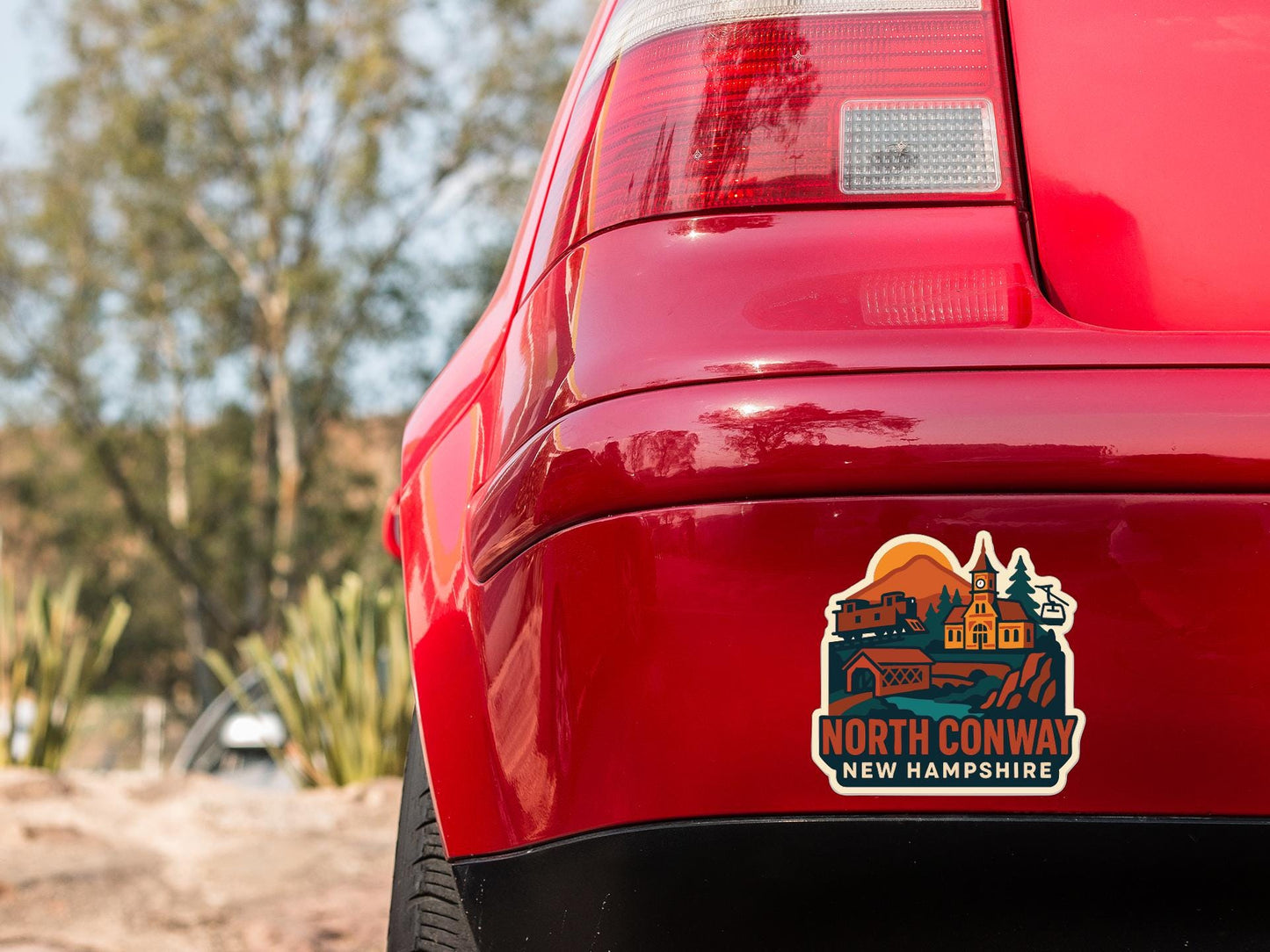 the rear end of a red car with a sticker on the trunk that says "NORTH CONWAY NEW HAMPSTEAD".